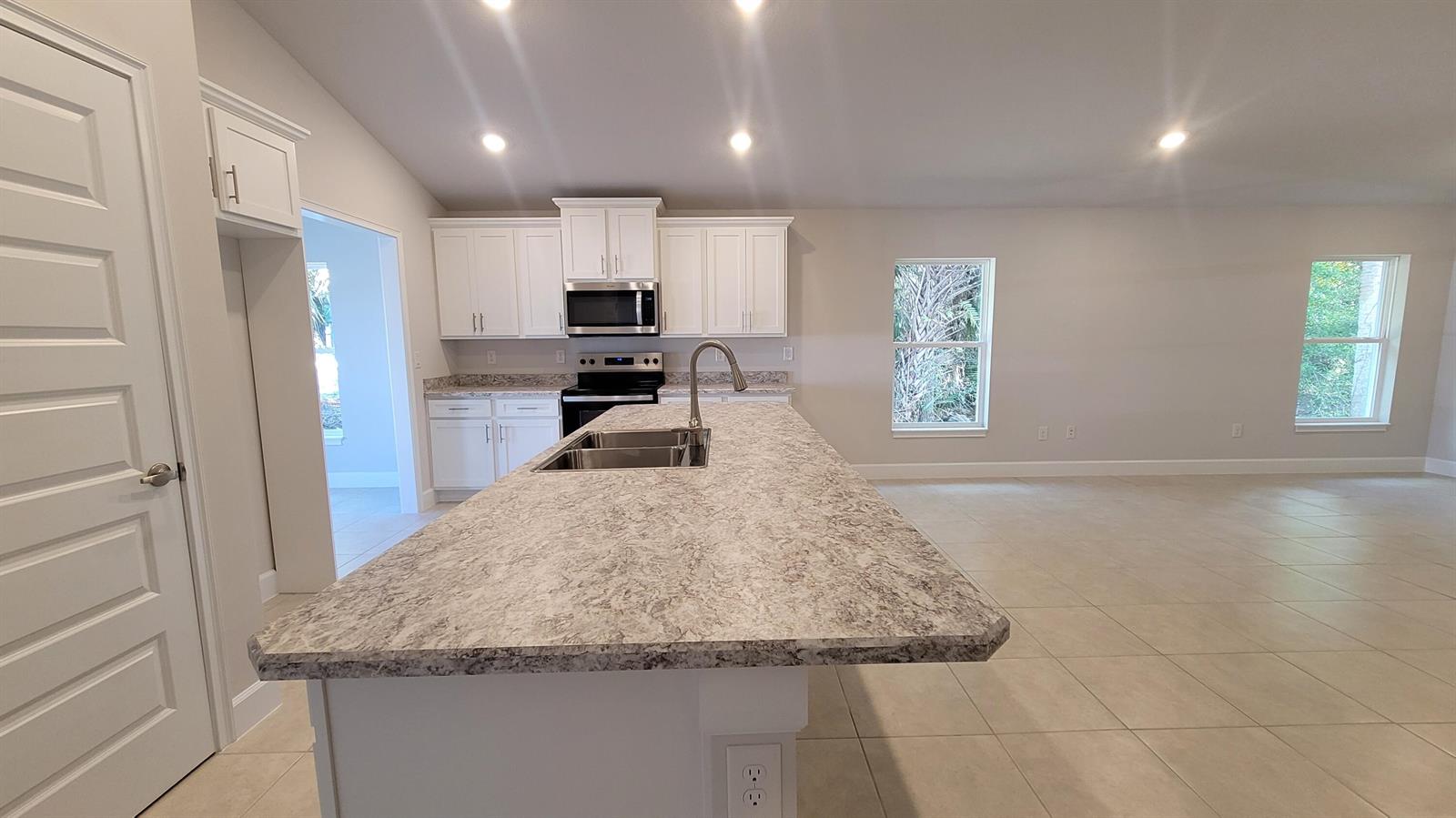 A kitchen features white cabinets, a granite-look island with a sink, and tile flooring — 8844 Waterstone Boulevard, Fort Pierce FL 34951, FORT PIERCE, FL