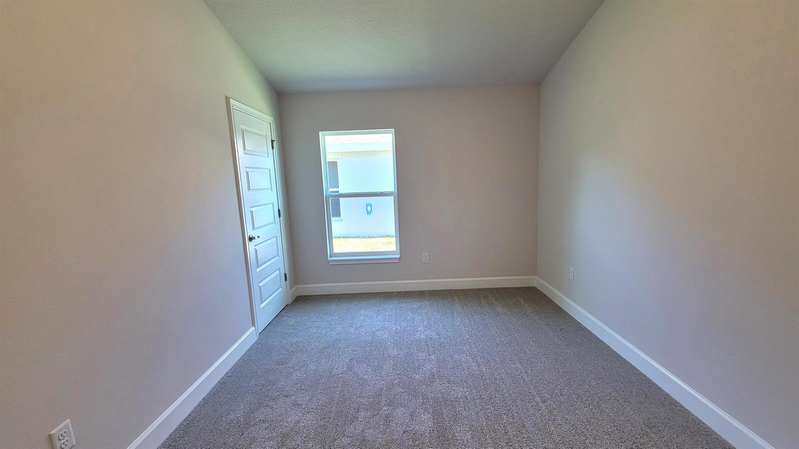 An empty bedroom features gray carpet, light-colored walls, a single window, and a white door — 8844 Waterstone Boulevard, Fort Pierce FL 34951, FORT PIERCE, FL