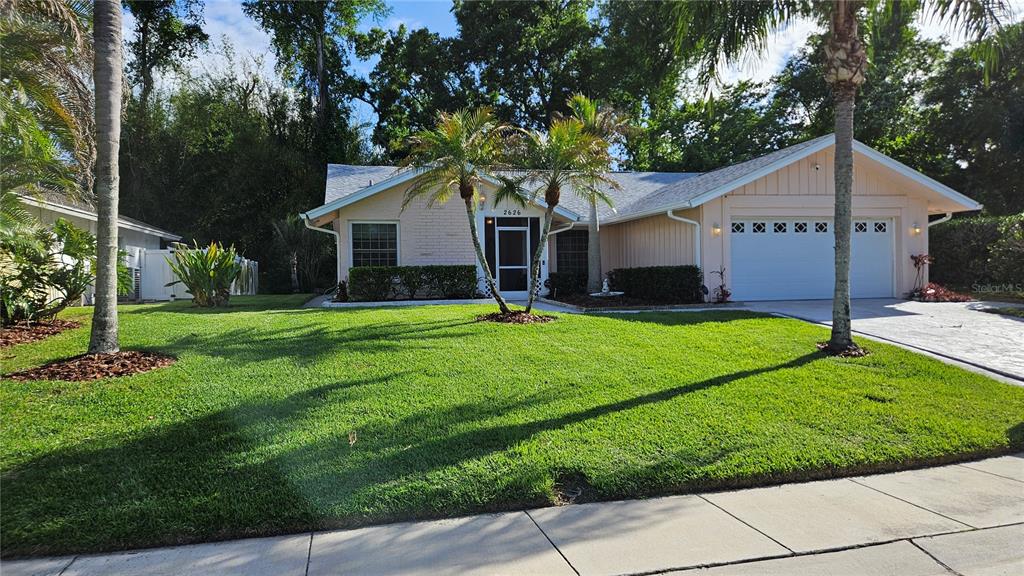 A single-story house with a light-colored exterior, a two-car garage, and a manicured front lawn — 2626 WENDOVER TERRACE, PALM HARBOR, FL