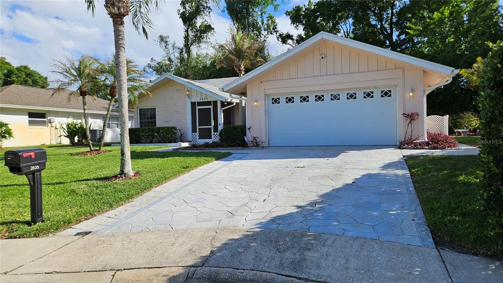 A single-story house with a white garage door, stone-patterned driveway, and a palm tree — 2626 WENDOVER TERRACE, PALM HARBOR, FL