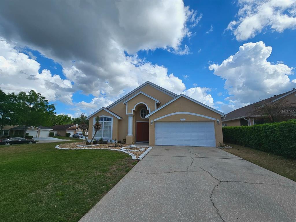 A single-story house with a tan stucco exterior, a white garage door, and a driveway — 15601 AUTUMN GLEN AVENUE, CLERMONT, FL