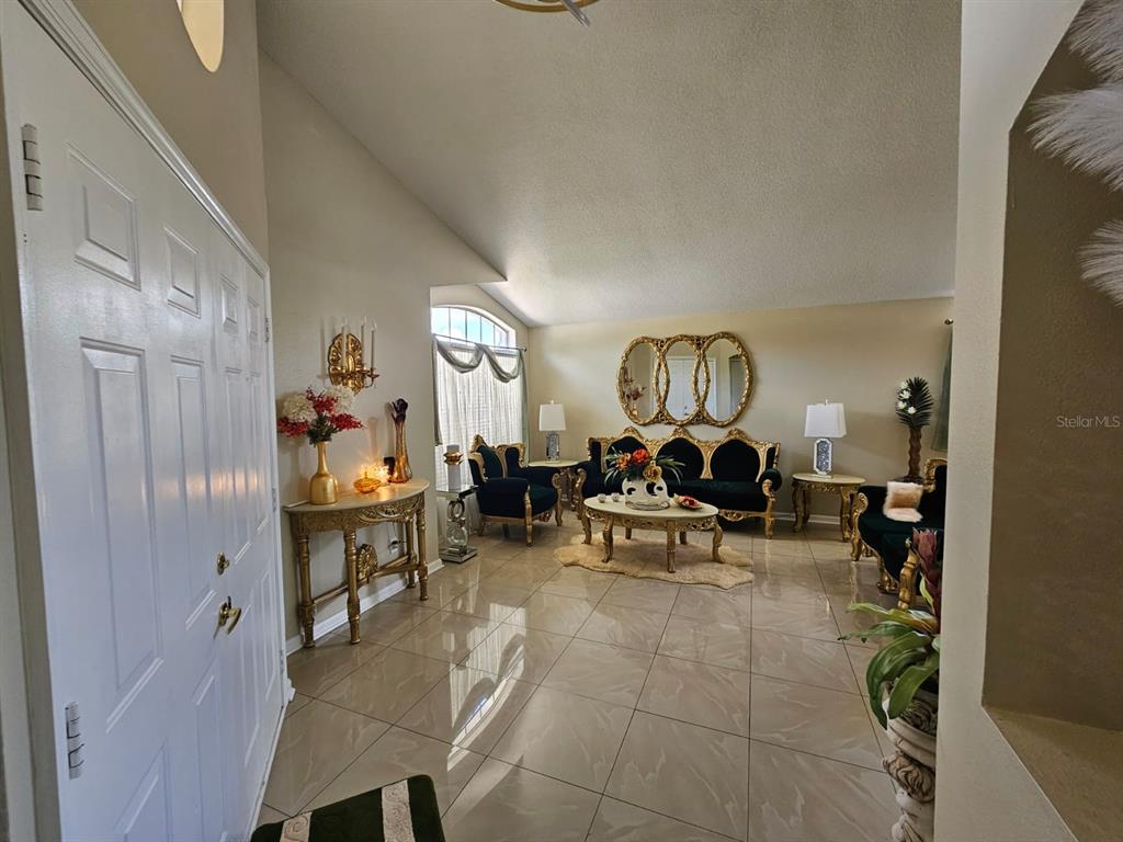A formal living room features tiled floors, gold-accented furniture, and a large arched window — 15601 AUTUMN GLEN AVENUE, CLERMONT, FL