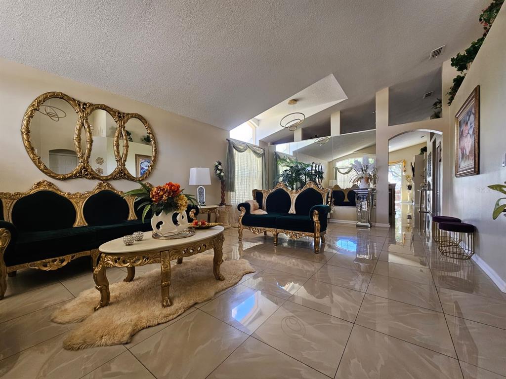 A formal living room features ornate gold-trimmed furniture, a large triple mirror, and tiled floors — 15601 AUTUMN GLEN AVENUE, CLERMONT, FL
