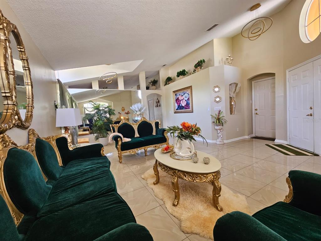 A living room features emerald green velvet sofas, a gold coffee table, and tiled floors — 15601 AUTUMN GLEN AVENUE, CLERMONT, FL