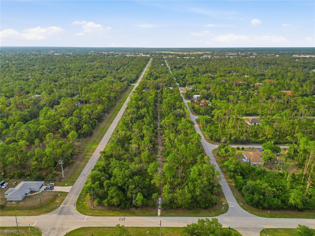 An aerial view shows a wooded lot situated between two paved roads in a residential area — 501 CHAMPION ST DRIVE, PORT CHARLOTTE, FL