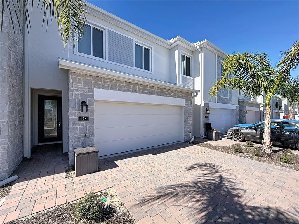 A two-story townhouse exterior features a stone facade, a white garage door, and paver driveway — 176 BOGEY DRIVE, DAVENPORT, FL