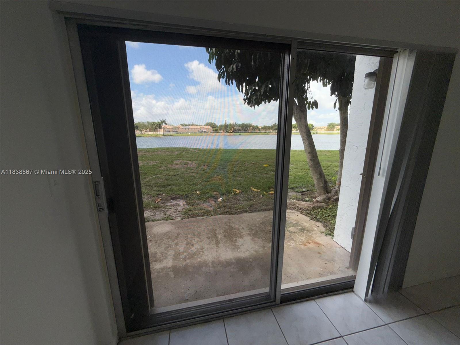 A sliding glass door opens to a concrete patio overlooking a lake and grassy yard — 8560 N Sherman Cir # 105, Miramar FL 33025, MIRAMAR, FL