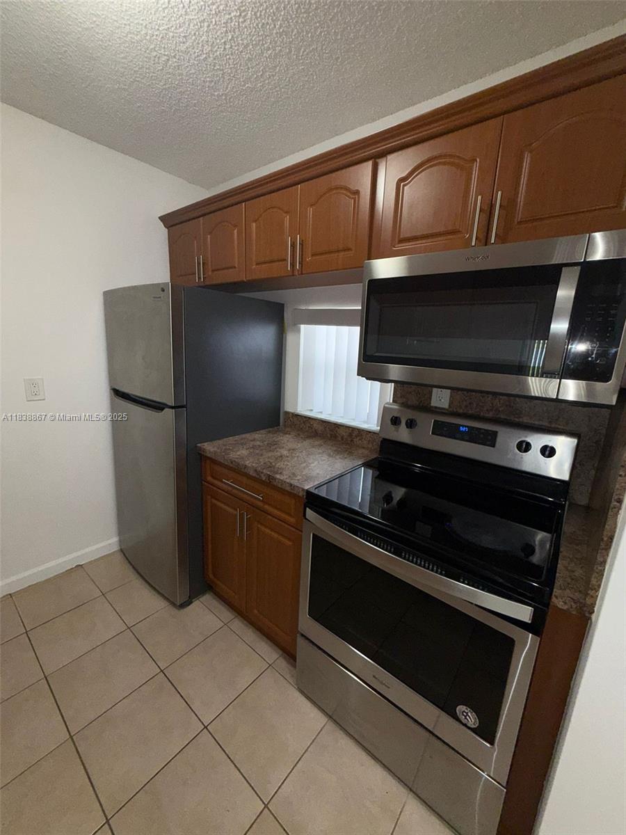 A kitchen features wood cabinets, stainless steel appliances, and tile flooring — 8560 N Sherman Cir # 105, Miramar FL 33025, MIRAMAR, FL