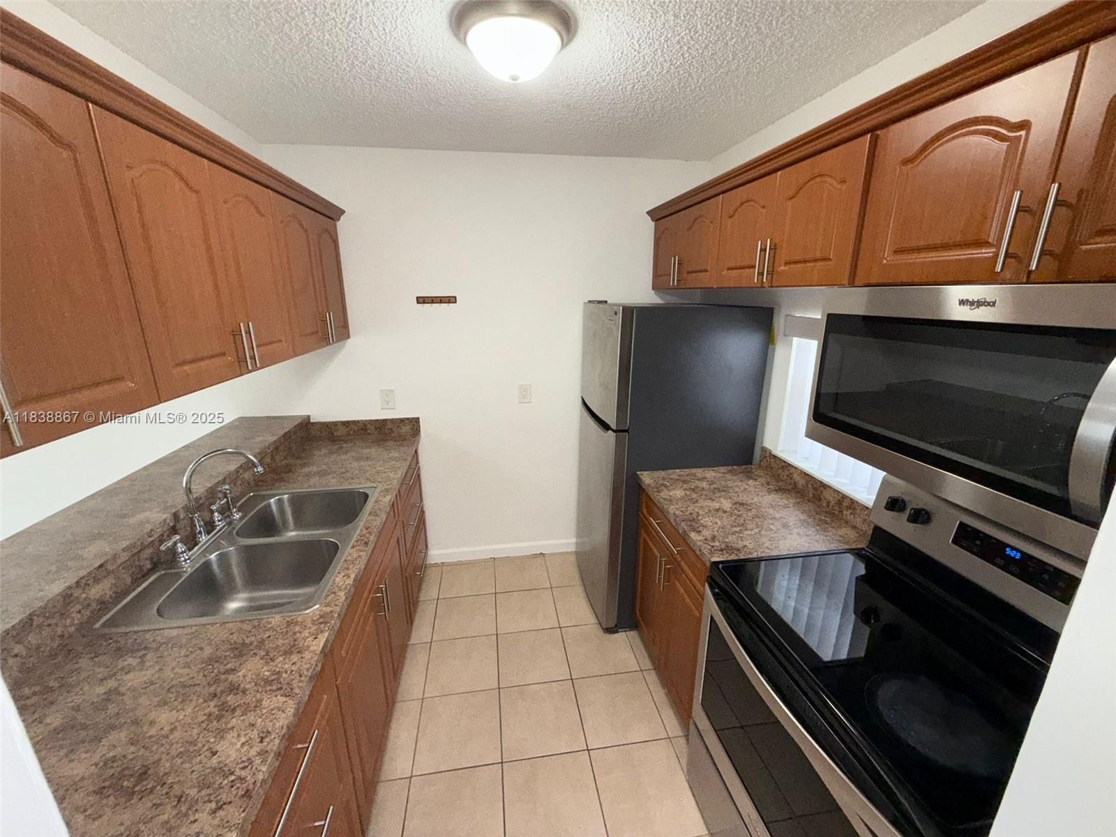 A galley kitchen features wood cabinets, laminate countertops, and stainless steel appliances — 8560 N Sherman Cir # 105, Miramar FL 33025, MIRAMAR, FL