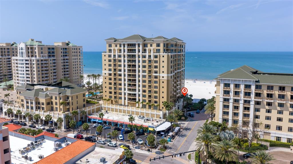 An aerial view shows several large, multi-story coastal resort buildings near a sandy beach — 11 BAYMONT STREET UNIT 302, CLEARWATER BEACH, FL