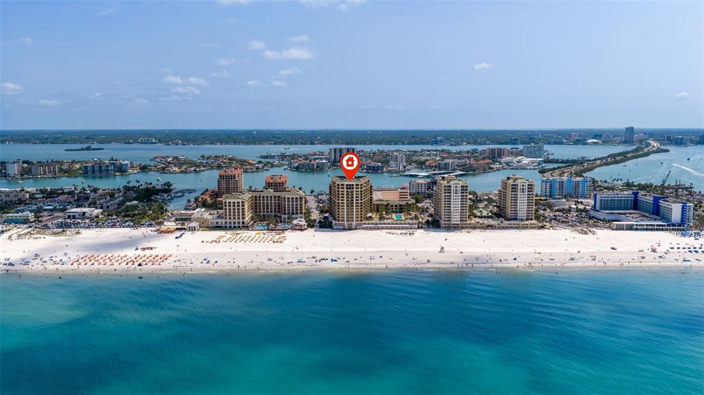 An aerial view shows a tall beachfront hotel surrounded by other buildings and the ocean — 11 BAYMONT STREET UNIT 302, CLEARWATER BEACH, FL