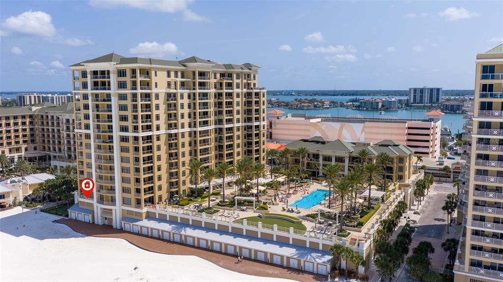 An aerial view of a multi-story beachside resort with a swimming pool and palm trees — 11 BAYMONT STREET UNIT 302, CLEARWATER BEACH, FL