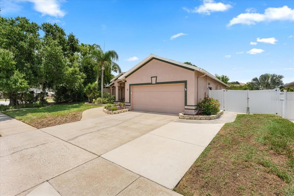 A single-story house with a beige stucco exterior, a two-car garage, and a white fence — 22804 WILLOW LAKES DRIVE, LUTZ, FL