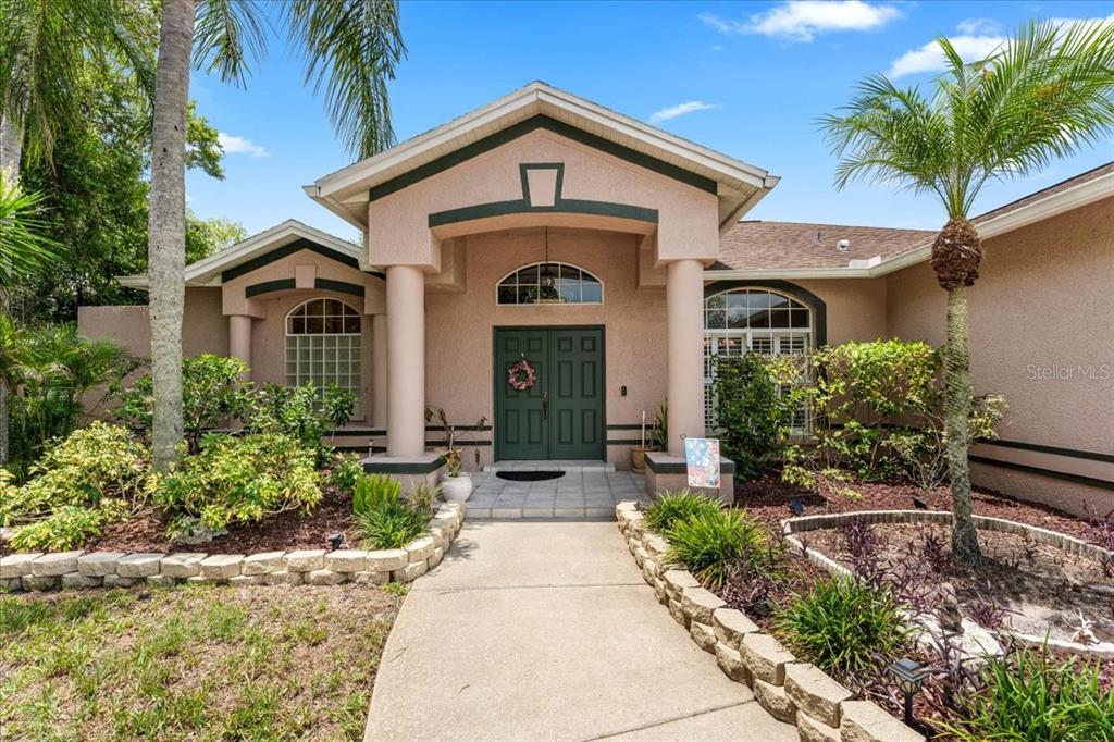 A tan house exterior features a covered entryway with columns and a dark green door — 22804 WILLOW LAKES DRIVE, LUTZ, FL