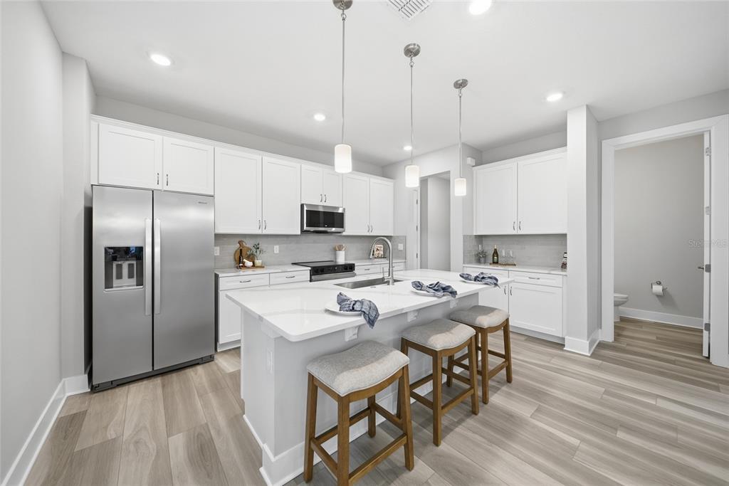 A modern kitchen features white cabinetry, a central island with bar seating, and stainless appliances — 31887 ANCHOR POINT DRIVE, WESLEY CHAPEL, FL