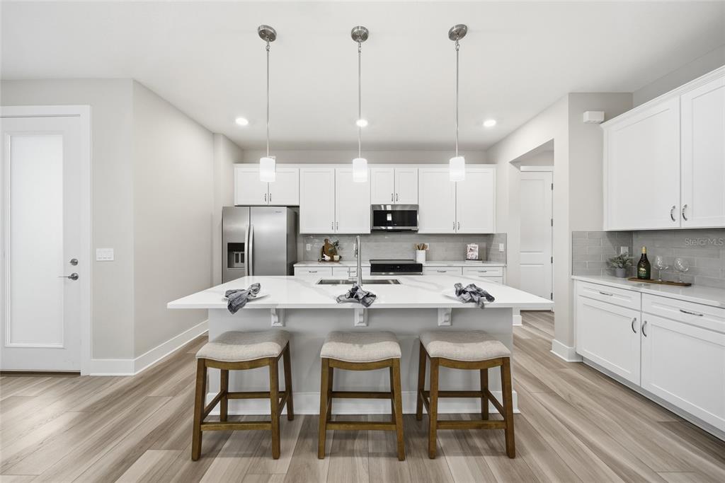 A modern kitchen features white cabinetry, a large quartz island with three stools, and wood-look flooring — 31887 ANCHOR POINT DRIVE, WESLEY CHAPEL, FL