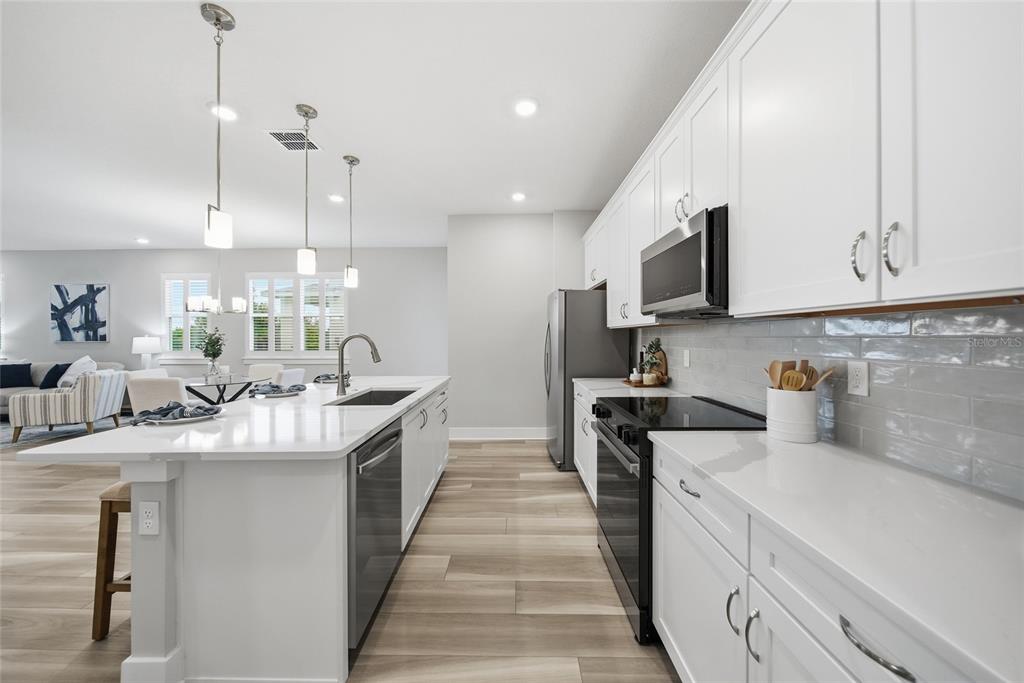A modern kitchen features white cabinets, quartz countertops, stainless steel appliances, and light wood flooring — 31887 ANCHOR POINT DRIVE, WESLEY CHAPEL, FL