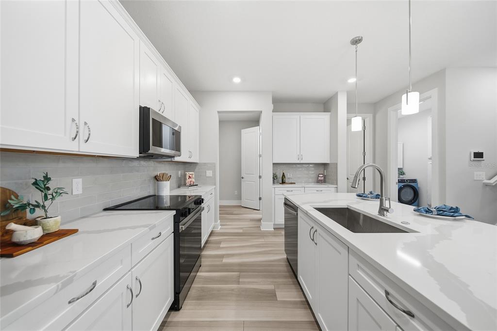 A modern kitchen features white cabinets, quartz countertops, a center island, and stainless steel appliances — 31887 ANCHOR POINT DRIVE, WESLEY CHAPEL, FL