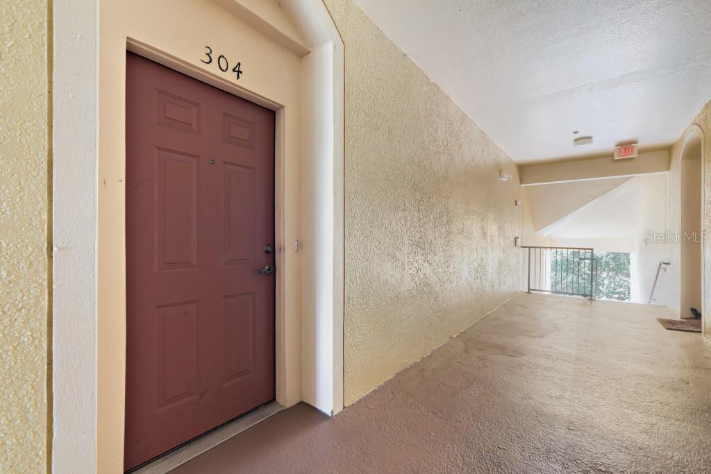 A red apartment door labeled 304 is located at the end of an outdoor hallway — 6380 CONTESSA DRIVE UNIT 304, ORLANDO, FL