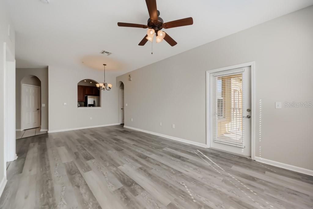 An empty living room features gray wood-look flooring, a ceiling fan, and a glass door — 6380 CONTESSA DRIVE UNIT 304, ORLANDO, FL