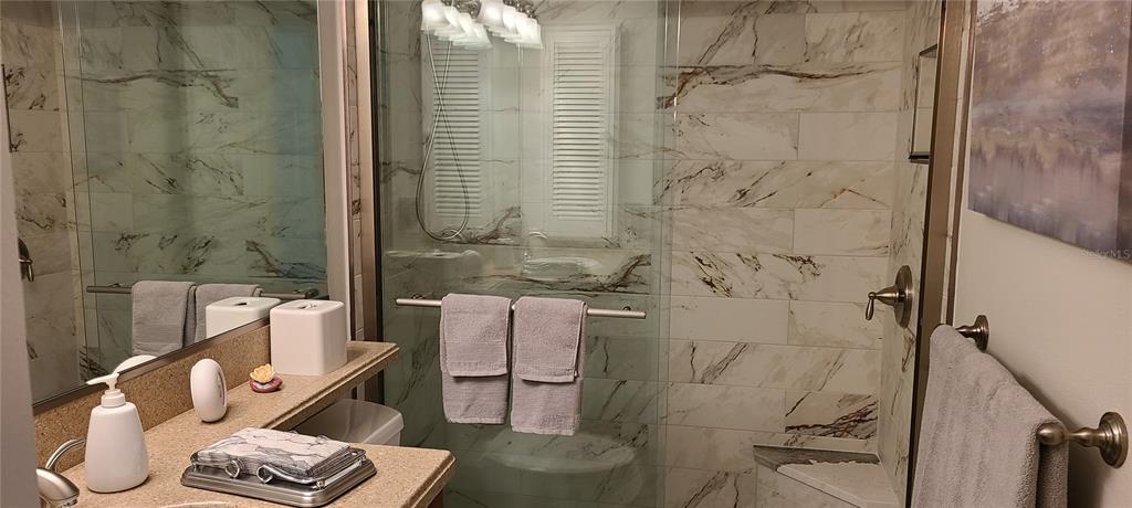 A bathroom features a glass-enclosed shower with marble-patterned tile and a vanity with a mirror — 1250 N PORTOFINO DRIVE UNIT 102MAR, SARASOTA, FL