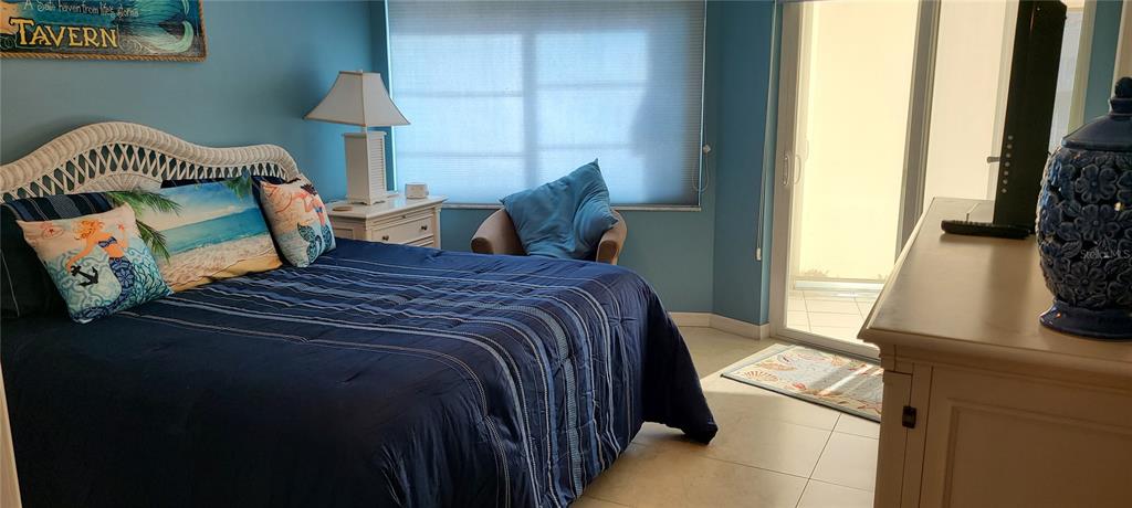 A bedroom features a bed with blue bedding, a wicker headboard, and a sliding glass door — 1250 N PORTOFINO DRIVE UNIT 102MAR, SARASOTA, FL