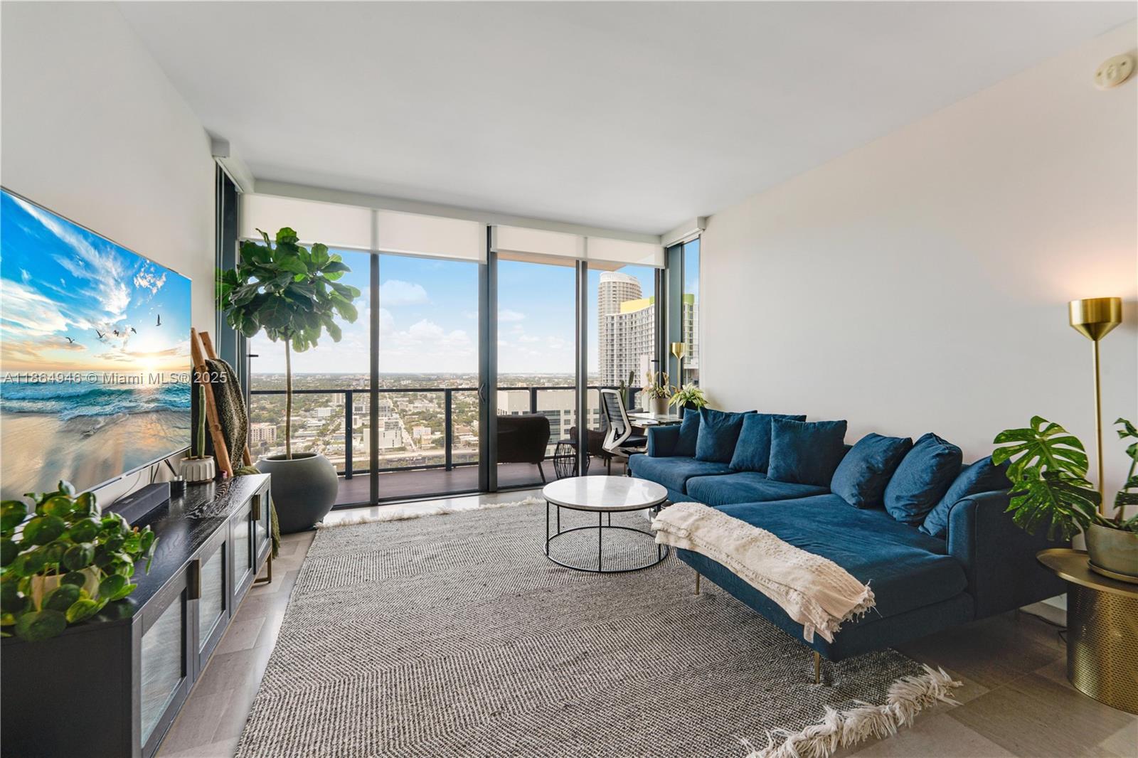 A modern living room features a blue sectional sofa, a television, and floor-to-ceiling windows — 88 SW 7th St # 2910, Miami FL 33130, MIAMI, FL