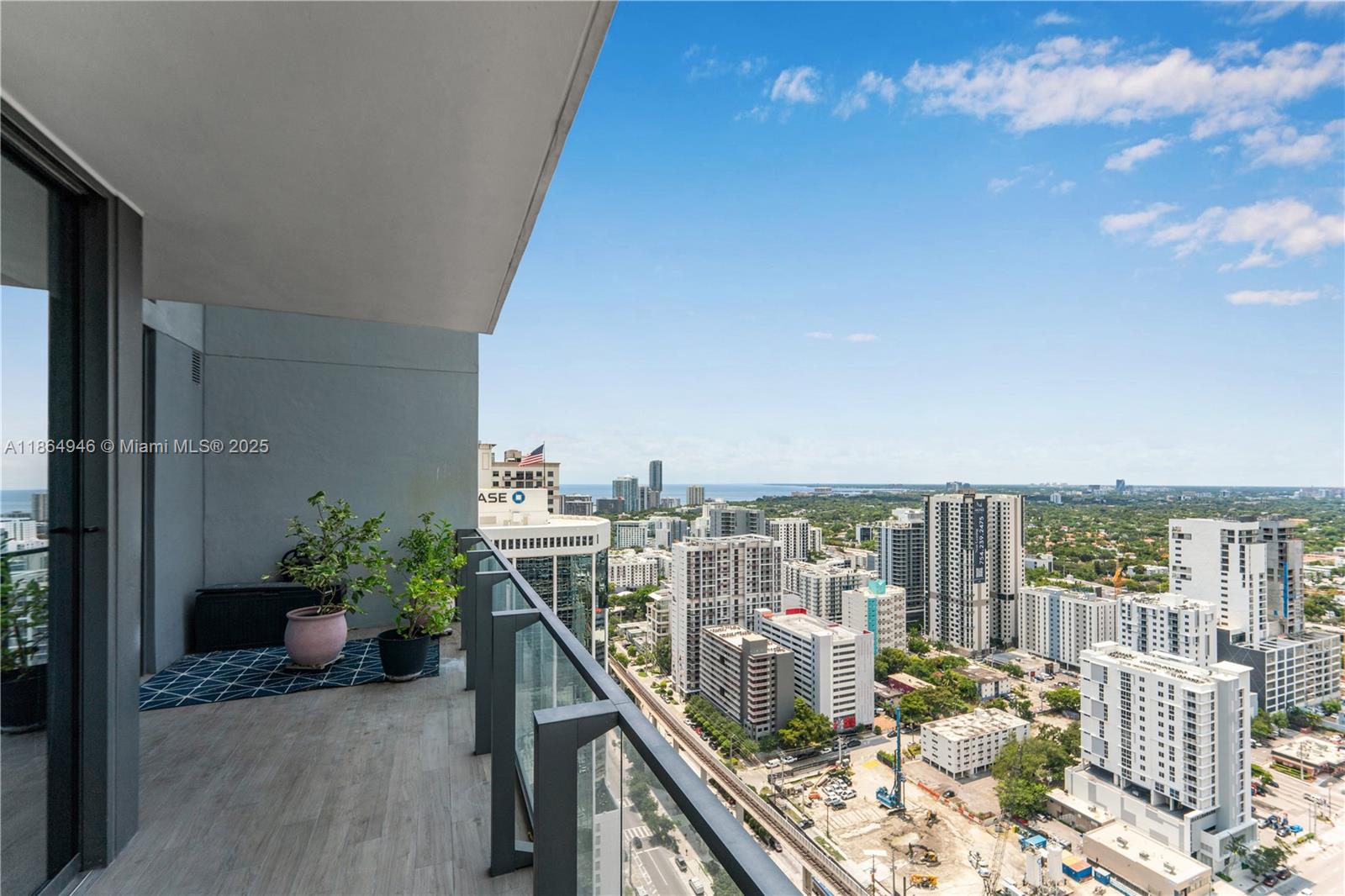 A high-rise balcony with wood-look flooring overlooks a dense urban cityscape under a blue sky — 88 SW 7th St # 2910, Miami FL 33130, MIAMI, FL