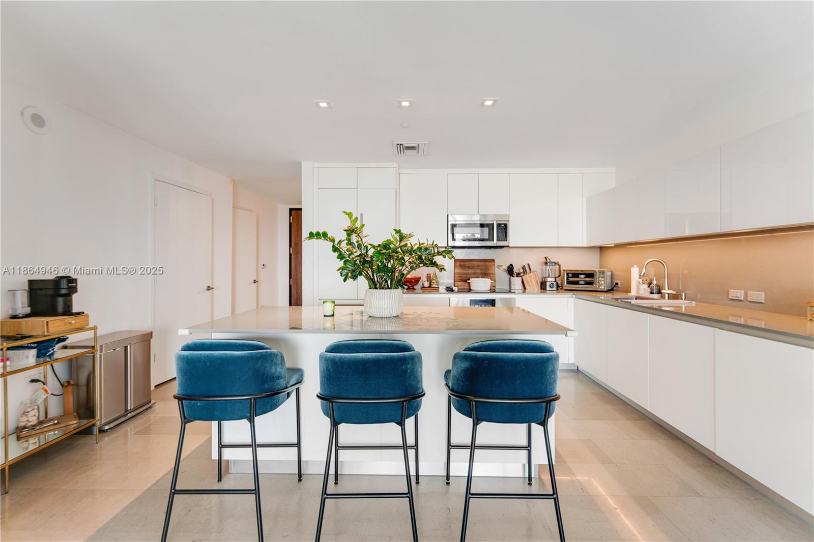 A modern kitchen features white cabinetry, a central island with three blue stools, and tile flooring — 88 SW 7th St # 2910, Miami FL 33130, MIAMI, FL