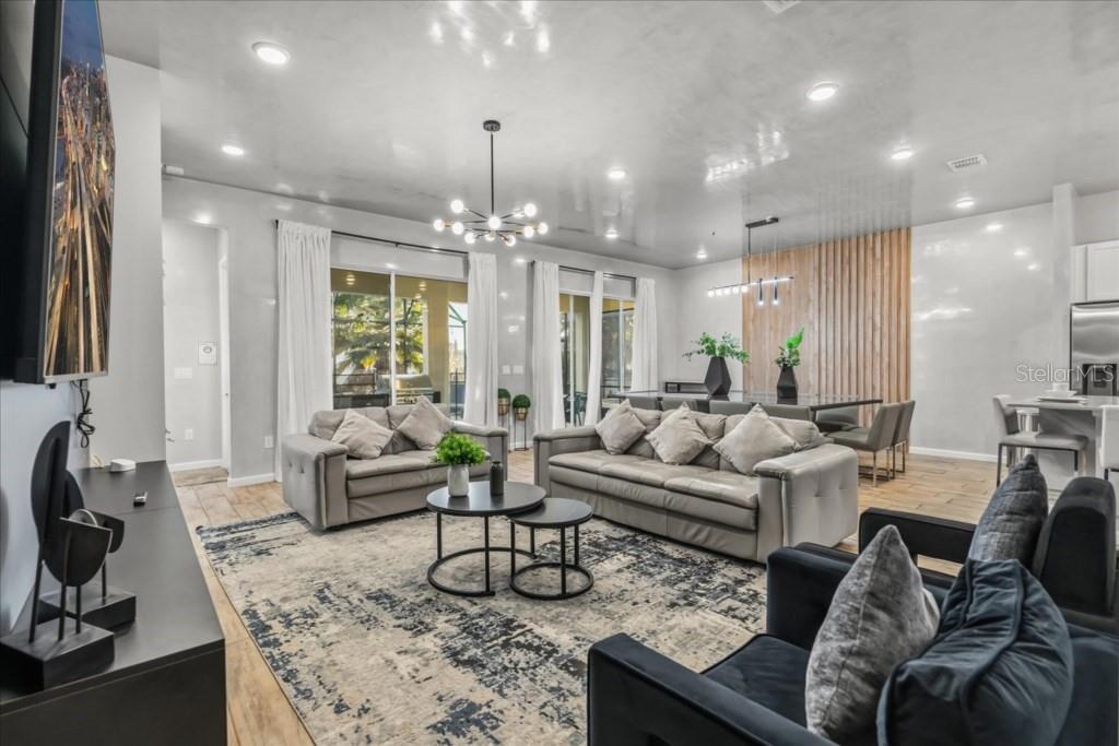 A modern open-concept living and dining area features a glossy ceiling, wood-slat wall, and tile — 2558 SHANTI DRIVE, KISSIMMEE, FL