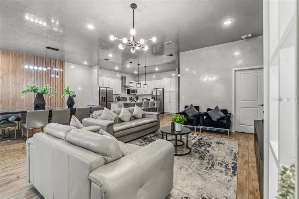 An open-concept living and dining area features a modern chandelier, gray sofas, and wood flooring — 2558 SHANTI DRIVE, KISSIMMEE, FL