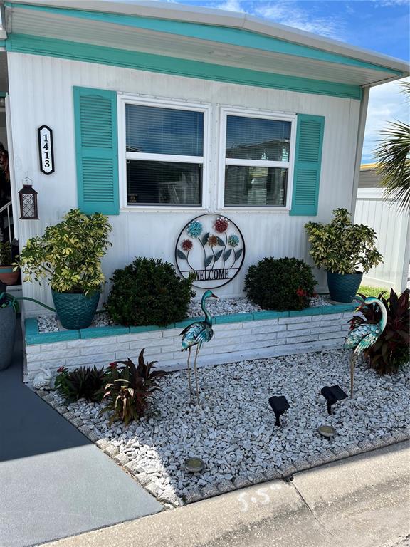 The exterior of a mobile home features white siding, teal shutters, and a landscaped rock garden — 1413 24TH AVENUE W, BRADENTON, FL
