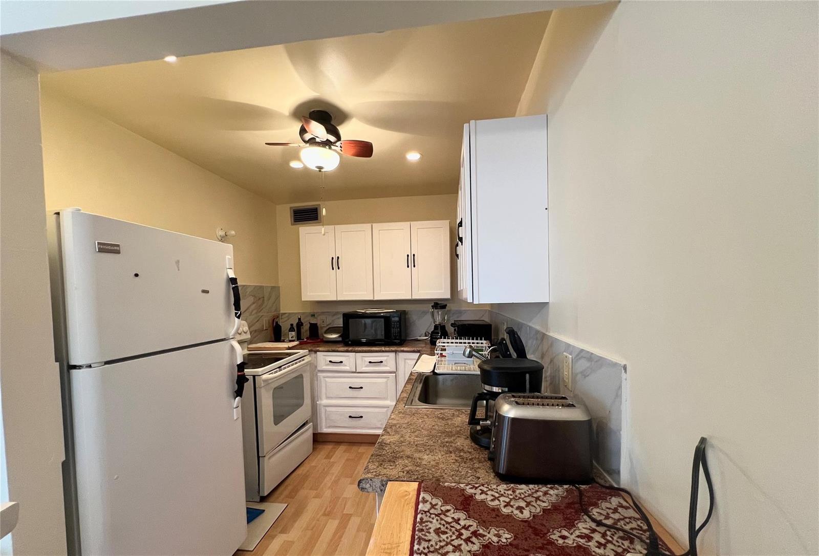 A galley kitchen features white cabinets, a white refrigerator, a stove, and brown countertops — 191 Markham I # 191, Deerfield Beach FL 33442, DEERFIELD BEACH, FL