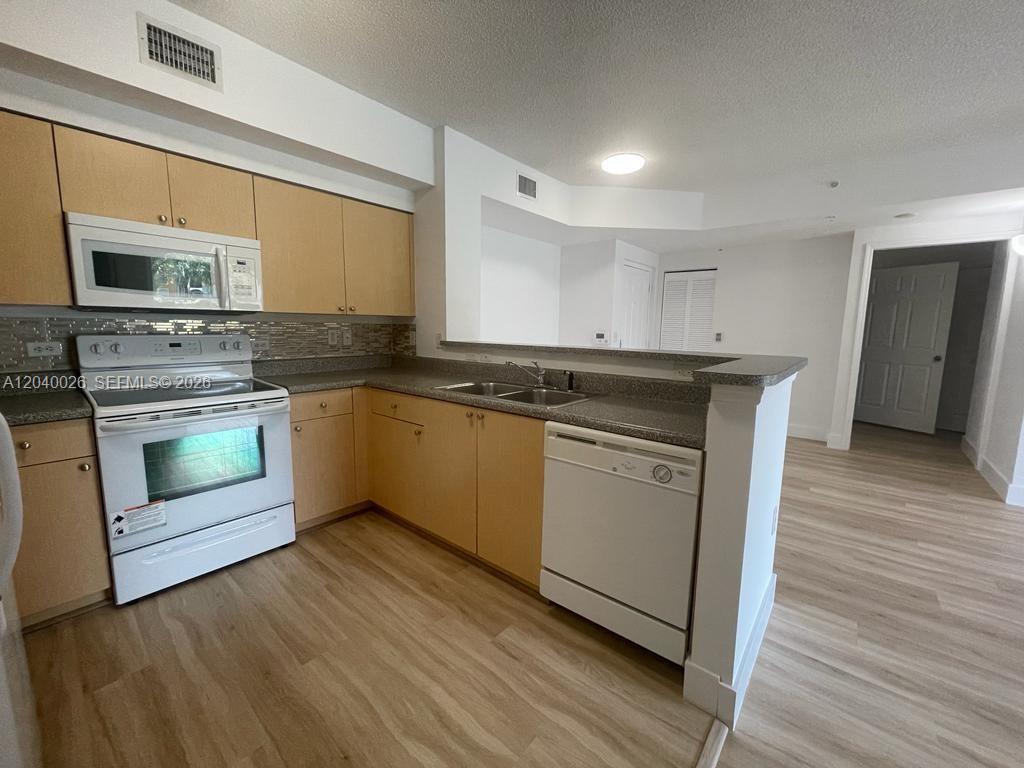A kitchen features light wood cabinets, white appliances, and a gray countertop with a backsplash — 2240 E Preserve Way # 104, Miramar FL 33025, MIRAMAR, FL