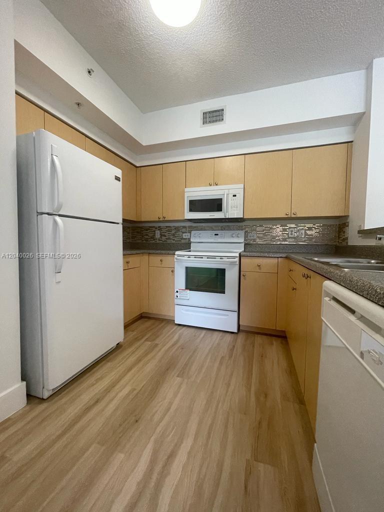 A kitchen features light wood cabinets, white appliances, and a tiled backsplash — 2240 E Preserve Way # 104, Miramar FL 33025, MIRAMAR, FL