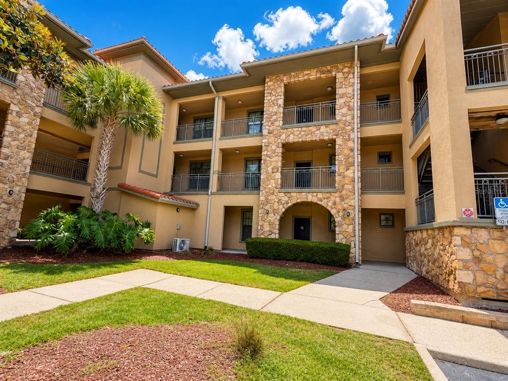 A three-story apartment building exterior features tan stucco walls, stone accents, and metal railings — 907 CHARO PARKWAY UNIT 915, DAVENPORT, FL