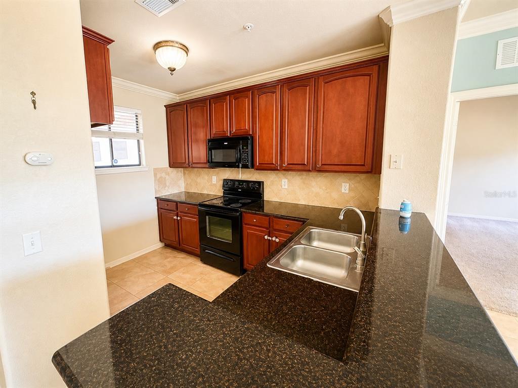 A kitchen features dark wood cabinets, granite countertops, a black stove, and a double sink — 907 CHARO PARKWAY UNIT 915, DAVENPORT, FL