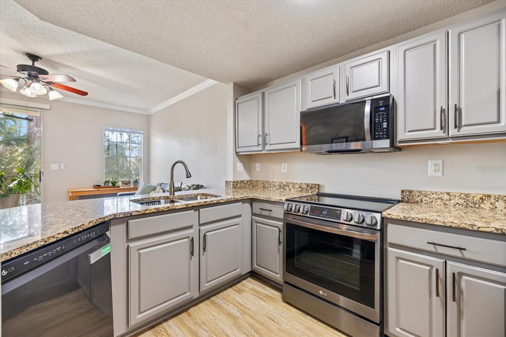 A kitchen with gray cabinets, granite countertops, and stainless steel appliances — 5552 BENTGRASS DRIVE UNIT 7-116, SARASOTA, FL