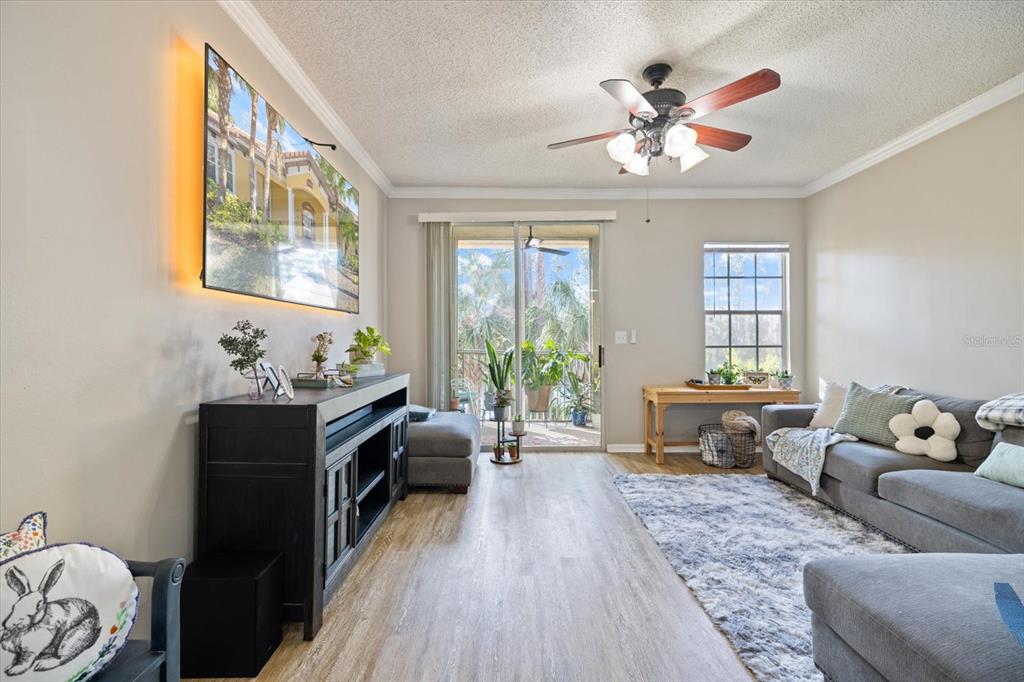 A living room features a grey sectional sofa, wood-look flooring, and a sliding glass door — 5552 BENTGRASS DRIVE UNIT 7-116, SARASOTA, FL
