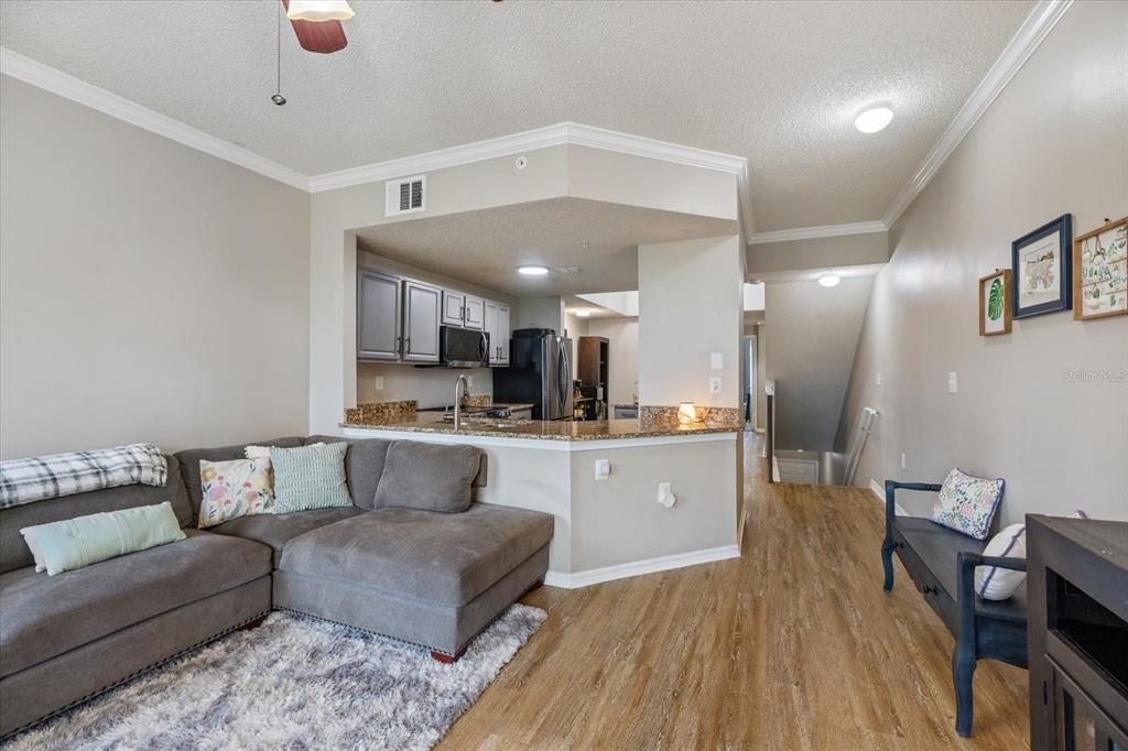 A living room with a sectional sofa, wood-look flooring, and an open kitchen pass-through — 5552 BENTGRASS DRIVE UNIT 7-116, SARASOTA, FL