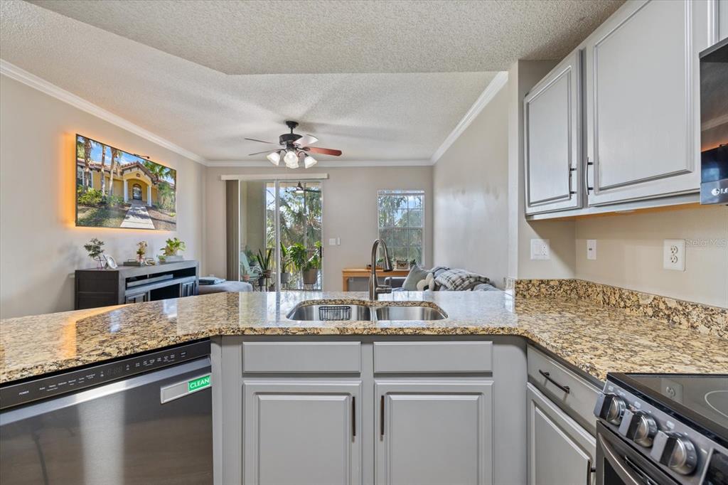 A kitchen with grey cabinets and granite countertops overlooks a living area with a balcony — 5552 BENTGRASS DRIVE UNIT 7-116, SARASOTA, FL