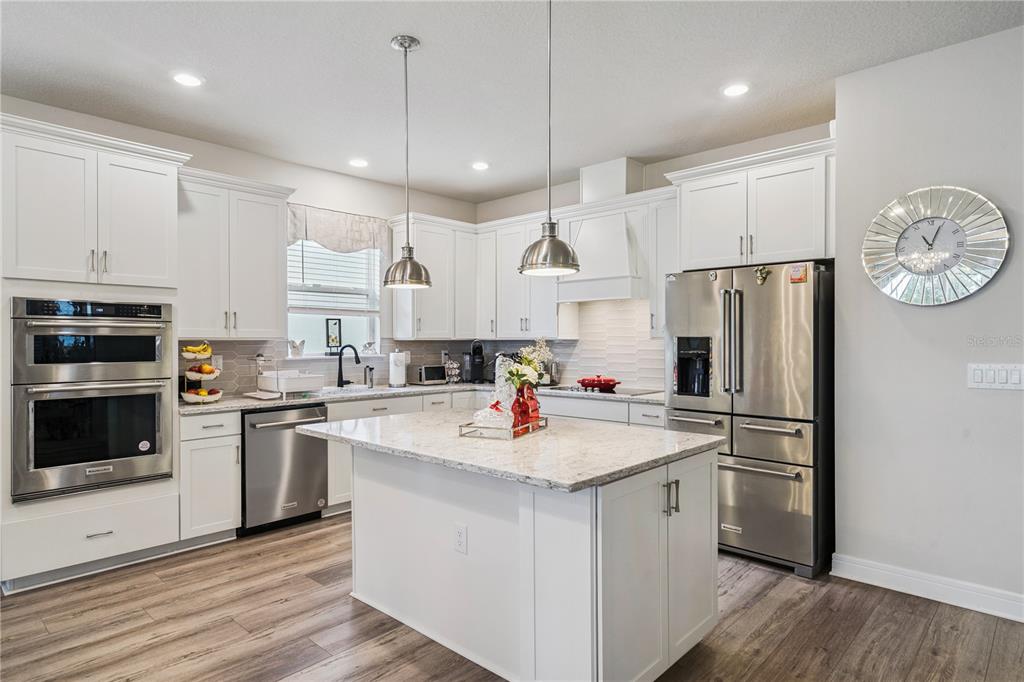 A modern kitchen features white cabinets, stainless steel appliances, a granite island, and wood flooring — 7798 SYRACUSE DRIVE, CLERMONT, FL