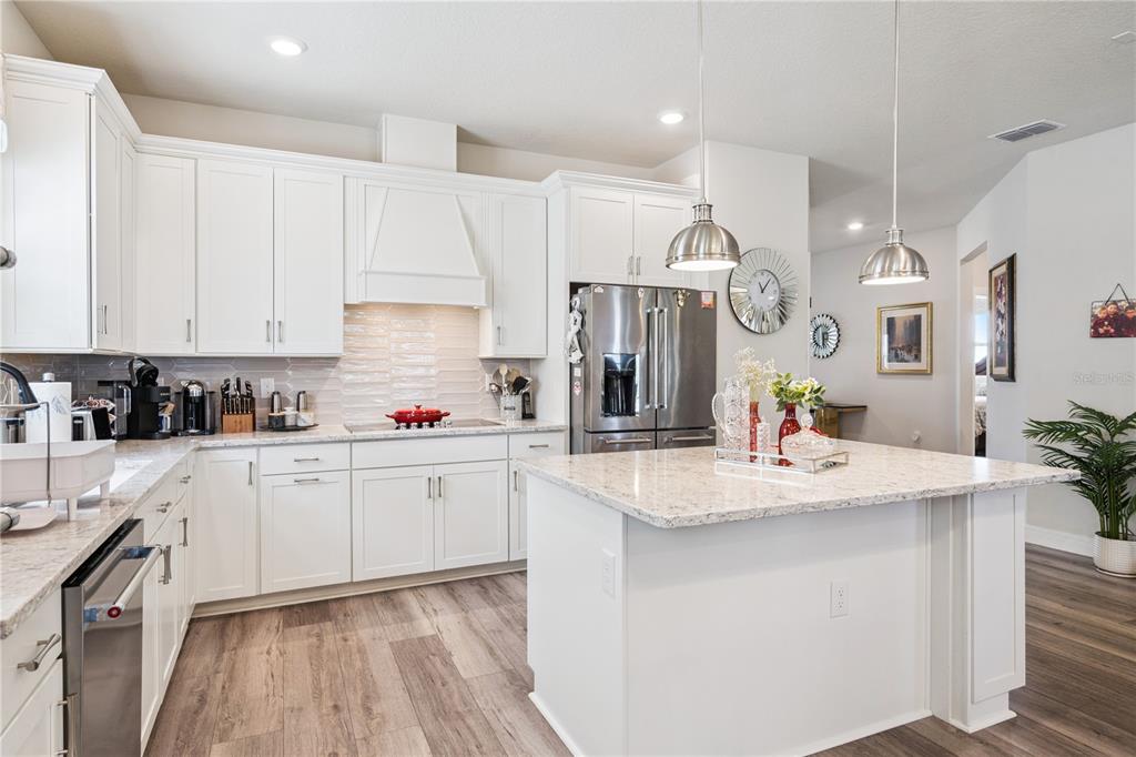 A modern kitchen features white cabinetry, granite countertops, stainless steel appliances, and a central island — 7798 SYRACUSE DRIVE, CLERMONT, FL