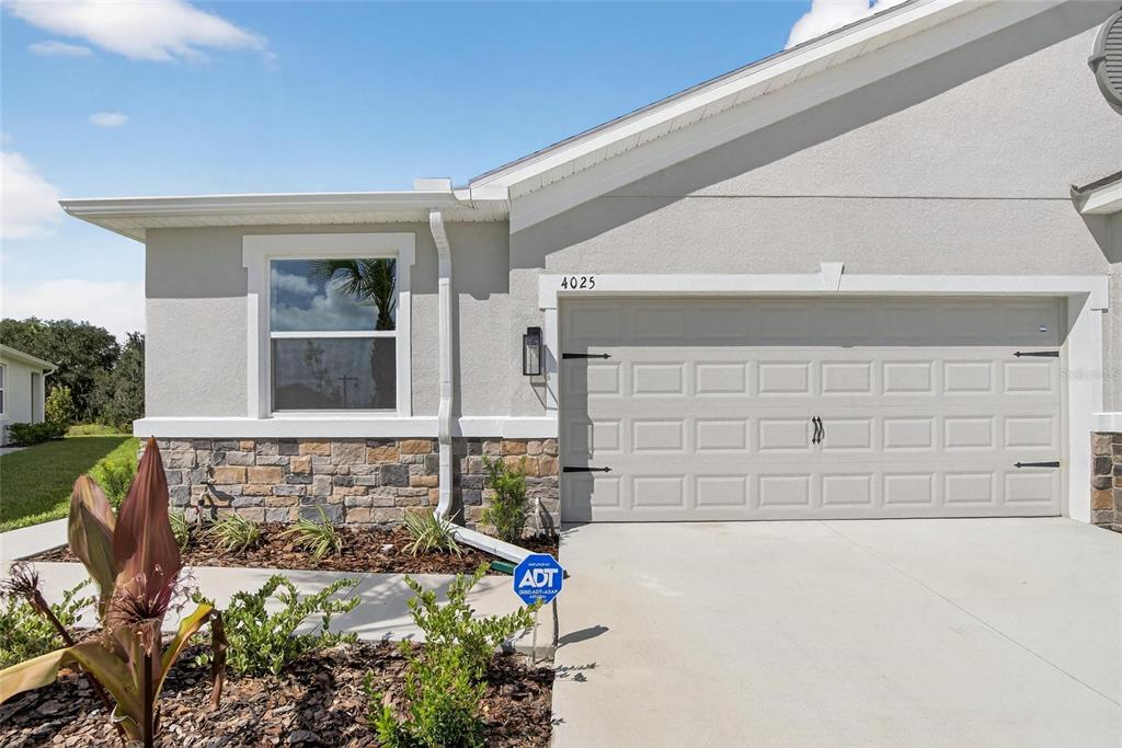 The exterior of a house features a stone-accented facade, a garage, and a small garden — 4025 WESTWOOD FIELDS LOOP, PLANT CITY, FL