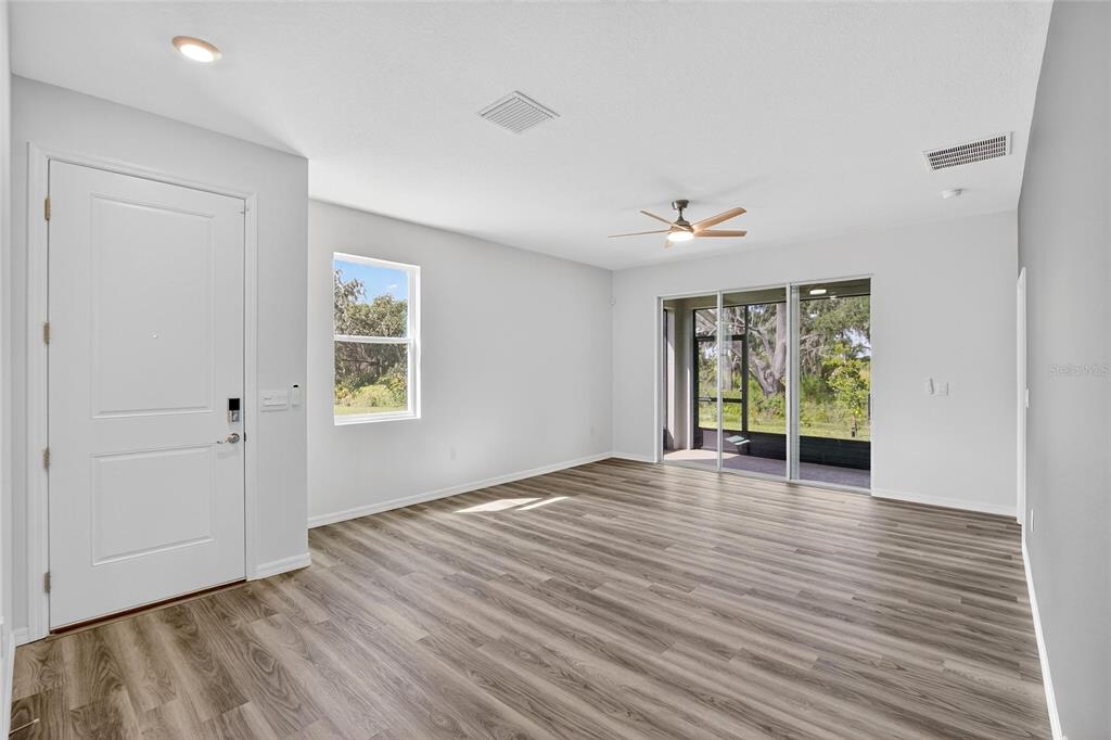 An empty living room features light gray walls, wood-look flooring, a ceiling fan, and sliding doors — 4025 WESTWOOD FIELDS LOOP, PLANT CITY, FL