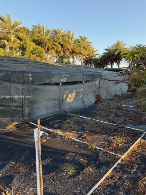 A black shade cloth structure sits over a field with irrigation pipes and palm trees — 17450 SW 208th St, Miami FL 33187, MIAMI, FL