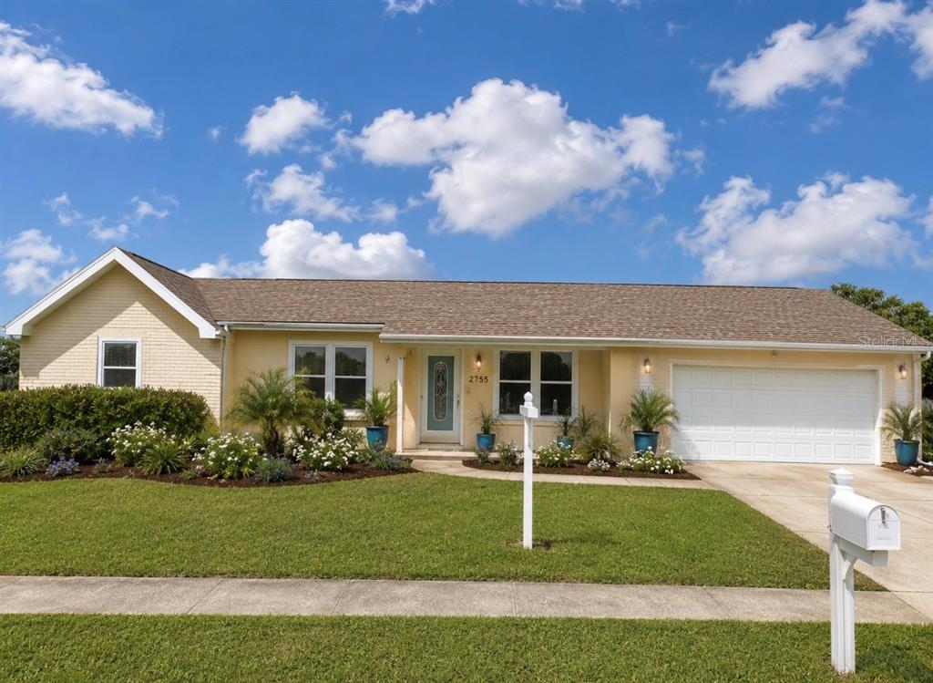 A single-story yellow house with a white garage and a front lawn under a blue sky — 2755 GREENDALE ROAD, NORTH PORT, FL