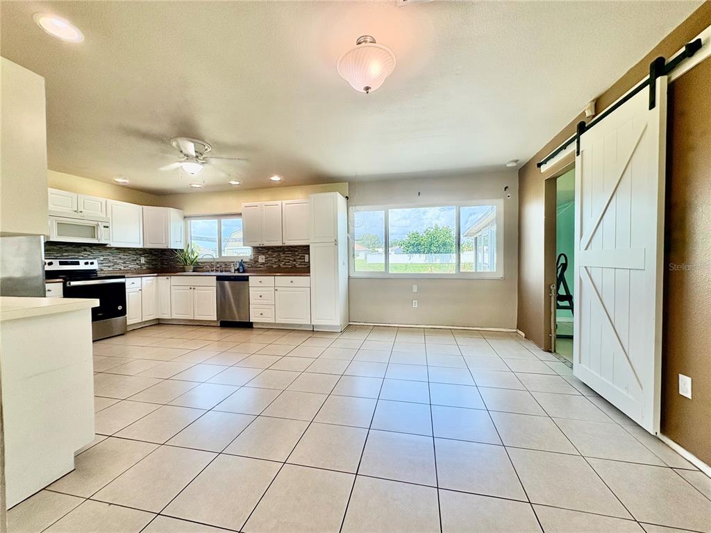 A kitchen with white cabinets, stainless steel appliances, and tile flooring, featuring a sliding barn door — 2755 GREENDALE ROAD, NORTH PORT, FL