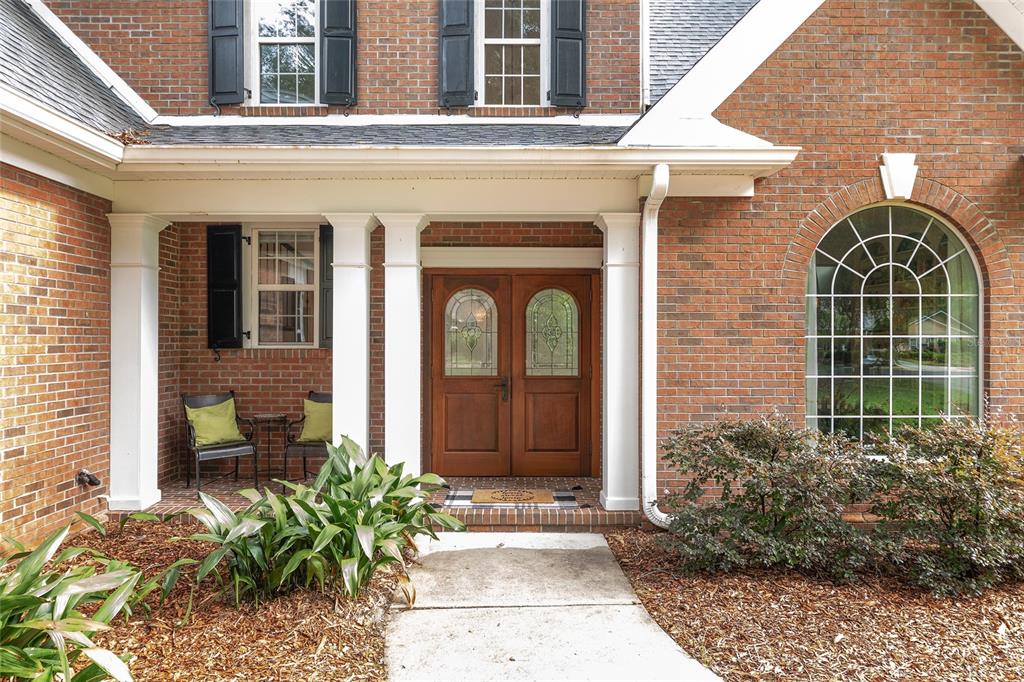A brick house exterior features a covered front porch with double wood doors and columns — 5512 NW 51ST AVENUE, GAINESVILLE, FL