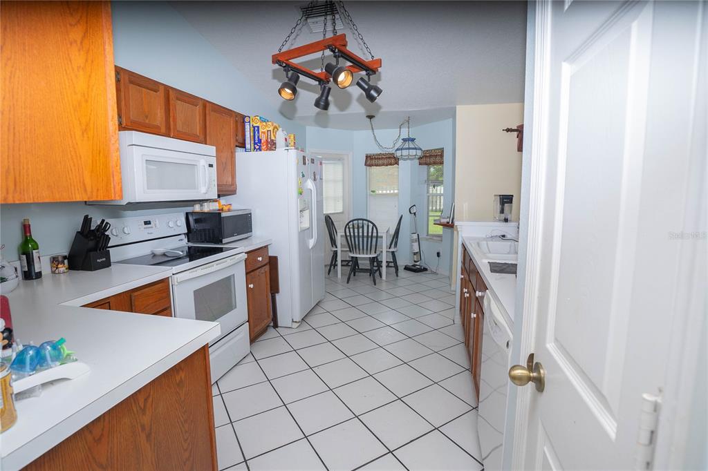 A kitchen with wood cabinets, white appliances, and a dining area with tiled floors — 2773 WOODSTREAM CIRCLE, KISSIMMEE, FL